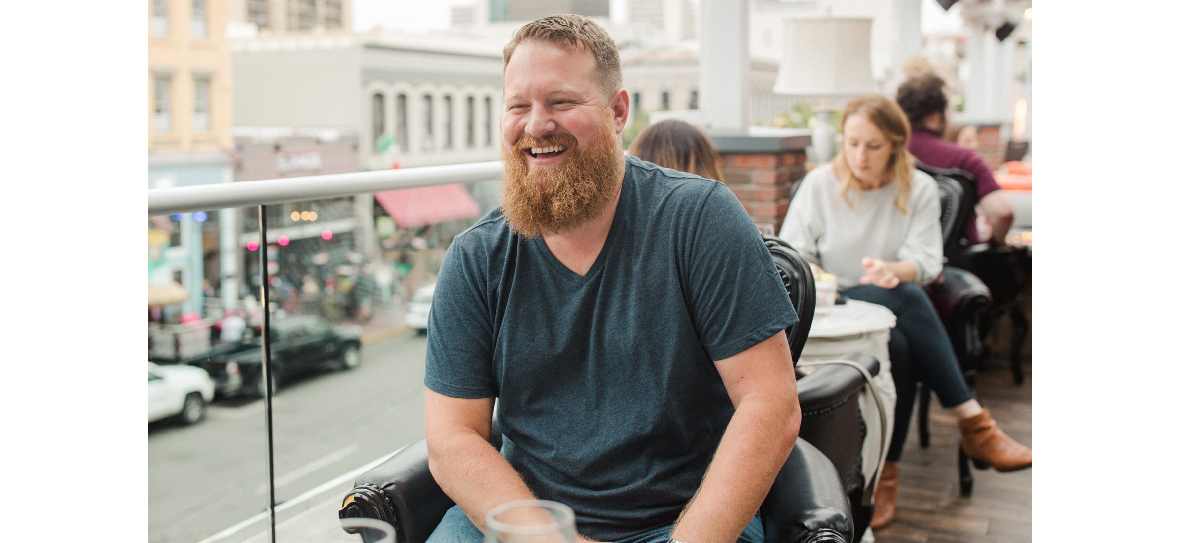 Chad sits at a cafe overlooking a street, laughing happily.